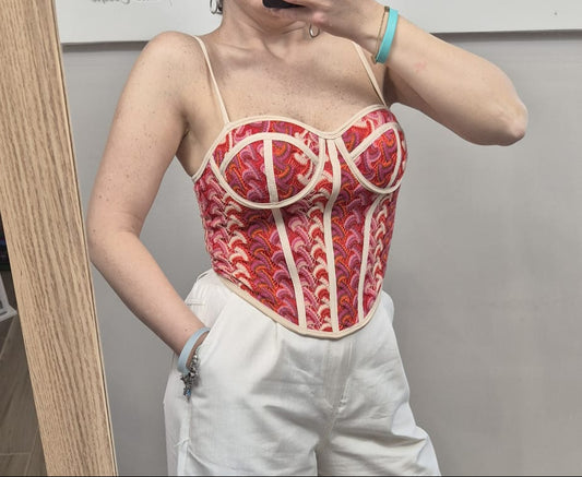 Top bustier donna rosa con fantasia rossa e bretelle sottili, abbinato a pantaloni bianchi.