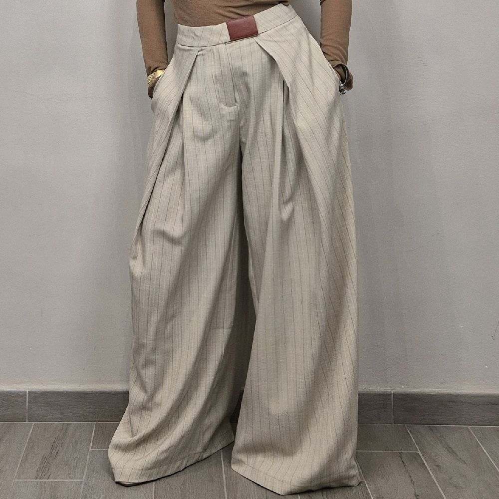 Pantaloni donna larghi a vita alta beige a righe, stile elegante, su pavimento grigio.