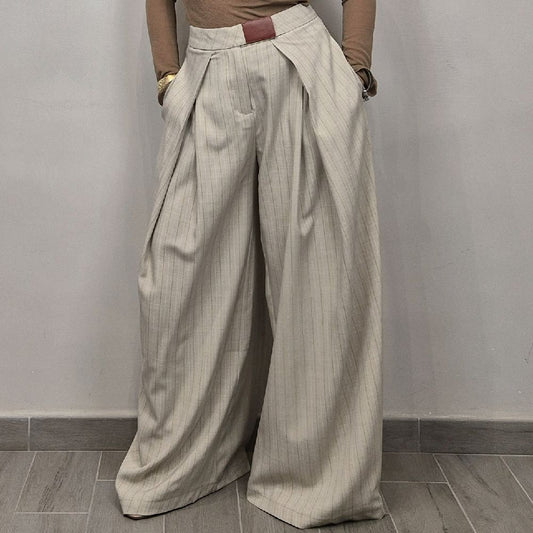 Pantaloni donna larghi a vita alta beige a righe, stile elegante, su pavimento grigio.