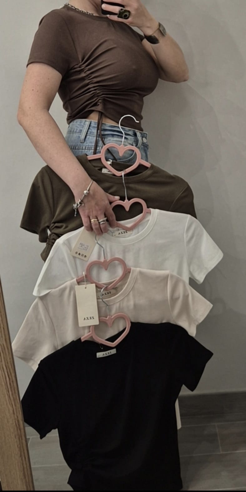 Magliette donna a manica corta con arricciatura, in diversi colori, esposte su grucce rosa
