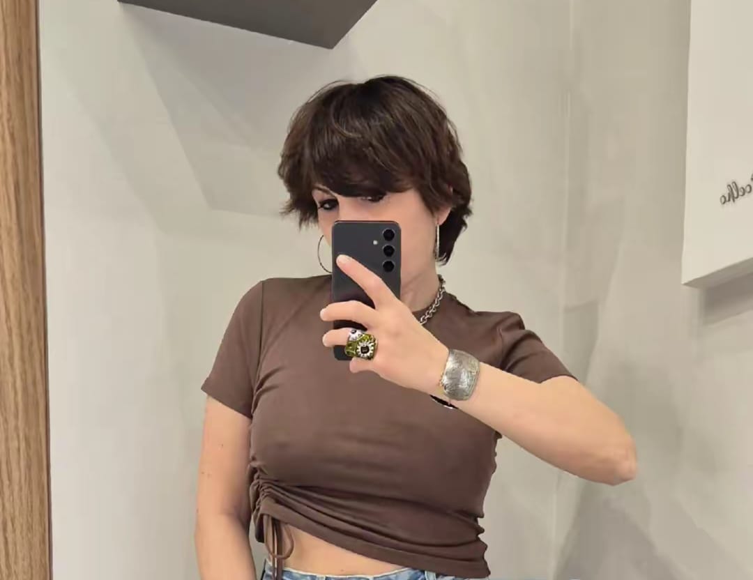 Donna con t-shirt marrone corta e jeans, selfie specchio in camerino, look moda casual