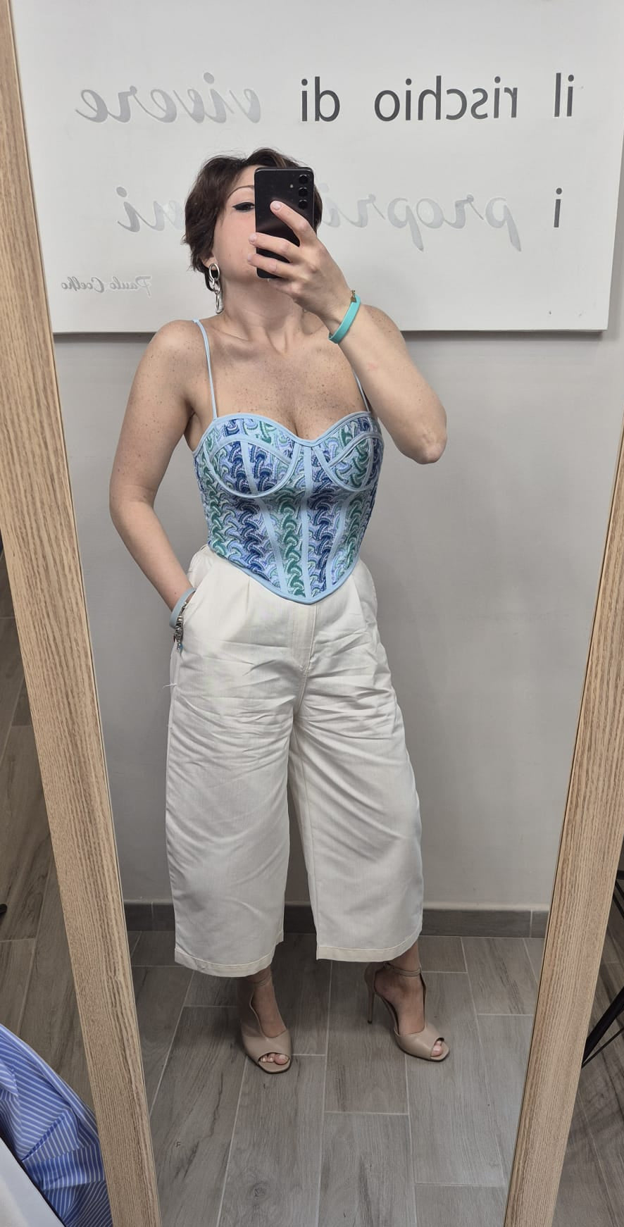 Donna indossa un bustier celeste con dettagli verdi e pantaloni bianchi larghi, look elegante.