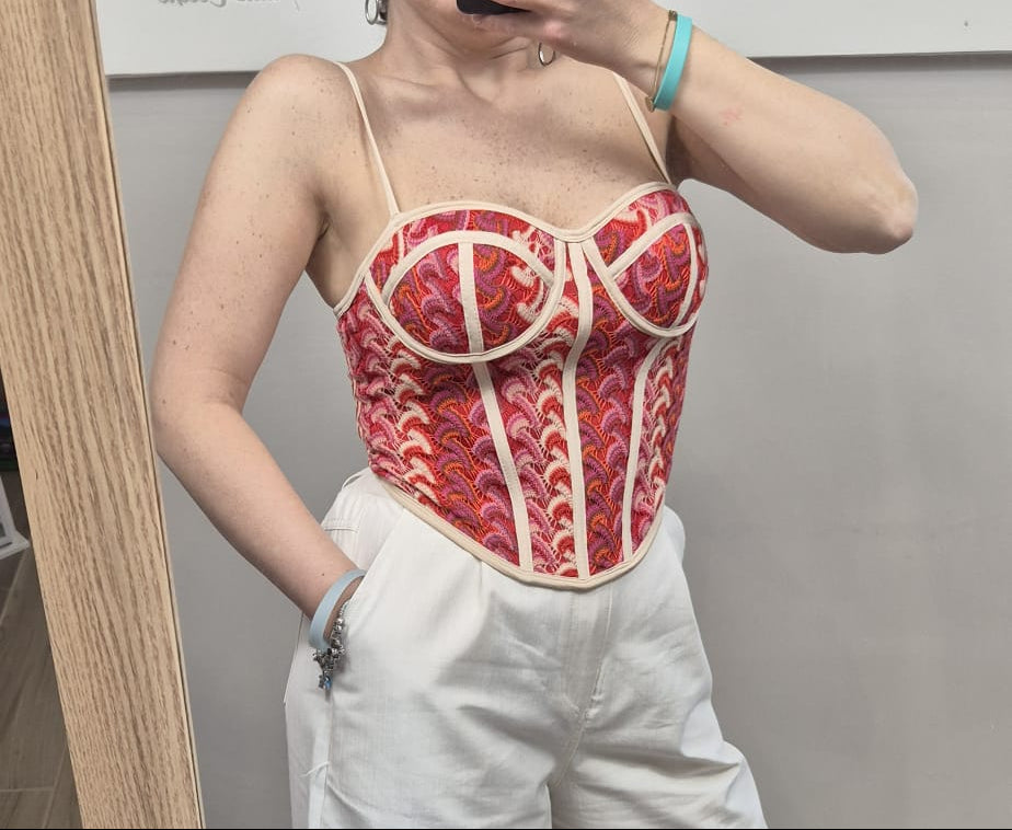 Top bustier donna rosa con fantasia rossa e bretelle sottili, abbinato a pantaloni bianchi.