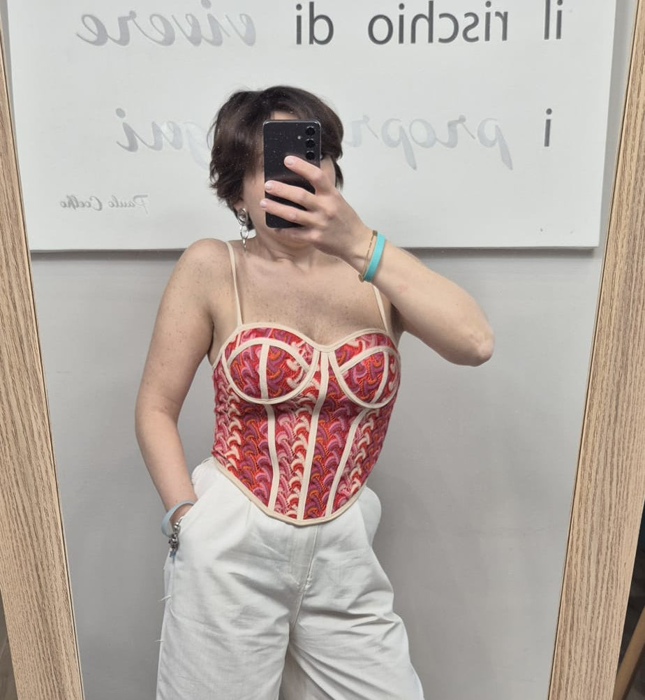 Donna indossa bustier colorato a fantasia rossa e pantaloni bianchi davanti allo specchio