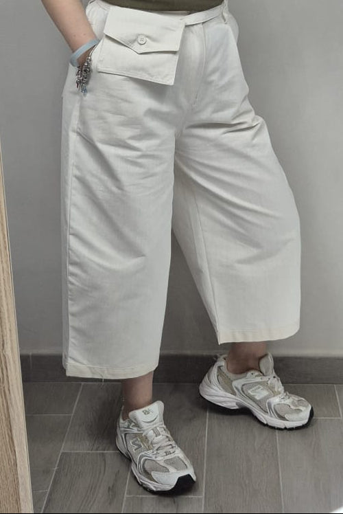 Pantaloni donna bianchi a gamba larga con tasca frontale, sneakers bianche, stile casual.