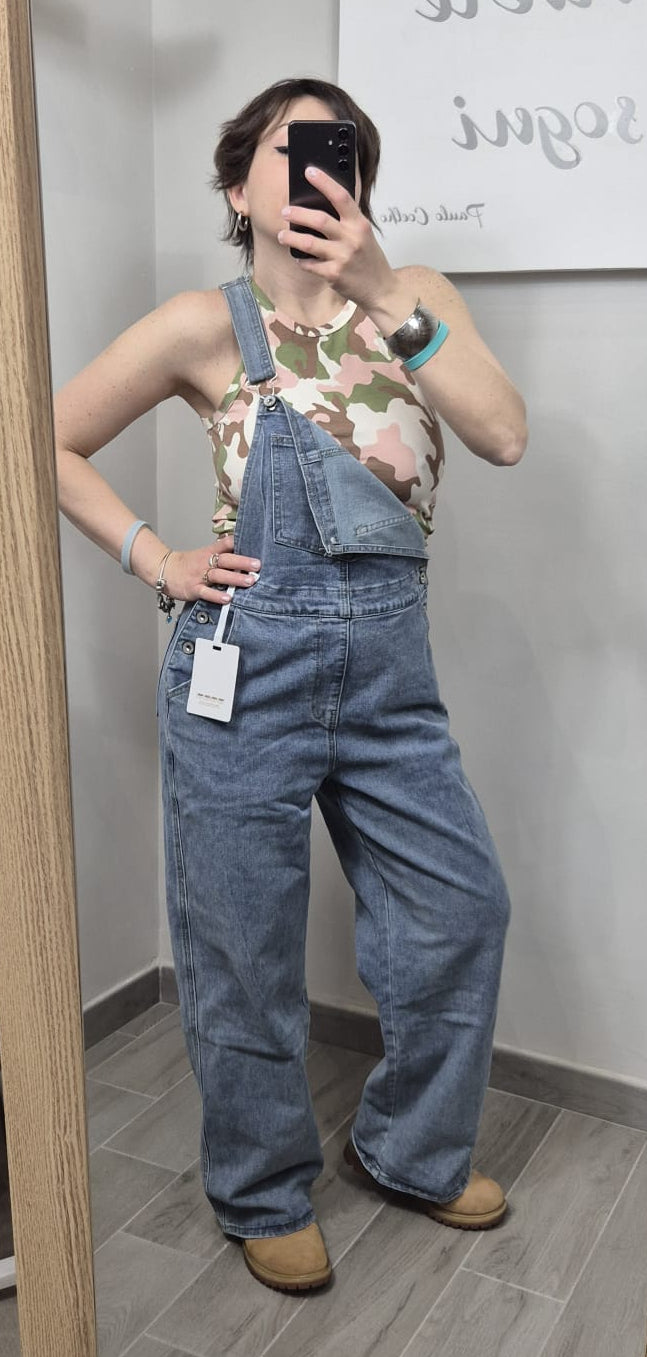 Donna indossa salopette di jeans larga e top smanicato camouflage, look casual trendy donna.