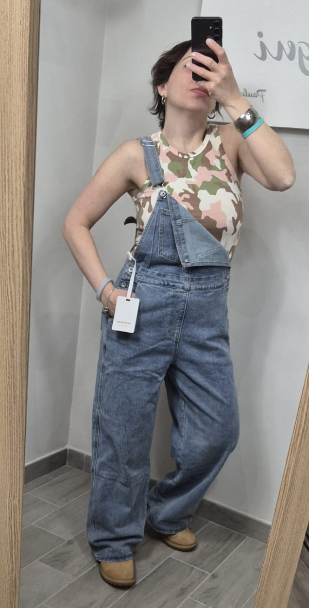 Donna indossa salopette di jeans oversize e top camouflage, posa davanti allo specchio